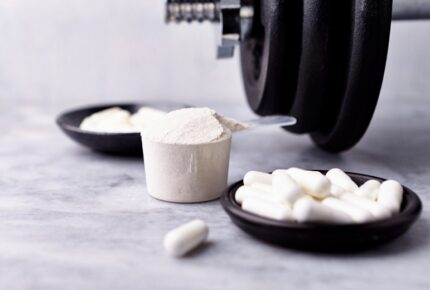 creatine capsules and powder in a scoop and dumbbell